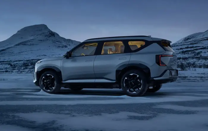 Kia EV5 AWD i silvergrå färg fotograferad från sidan i snöig vinterlandskap med berg i bakgrunden, upplyst kupé i varmt ljus